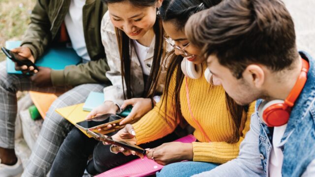 Students sitting together viewing content on their phones and tablets